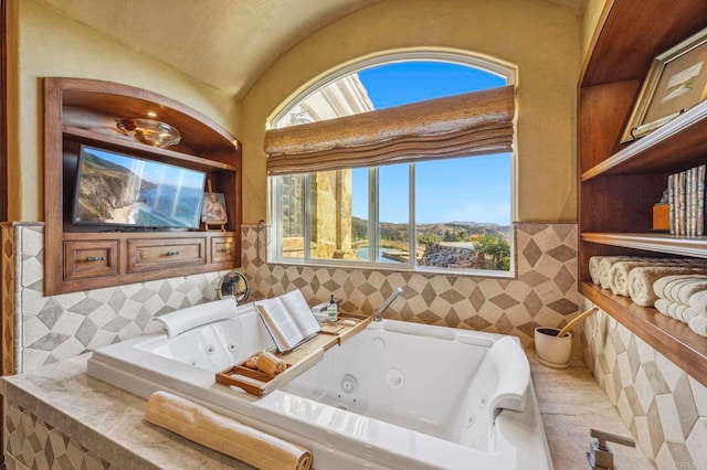 bathroom featuring a relaxing tiled tub, vaulted ceiling, and tile walls