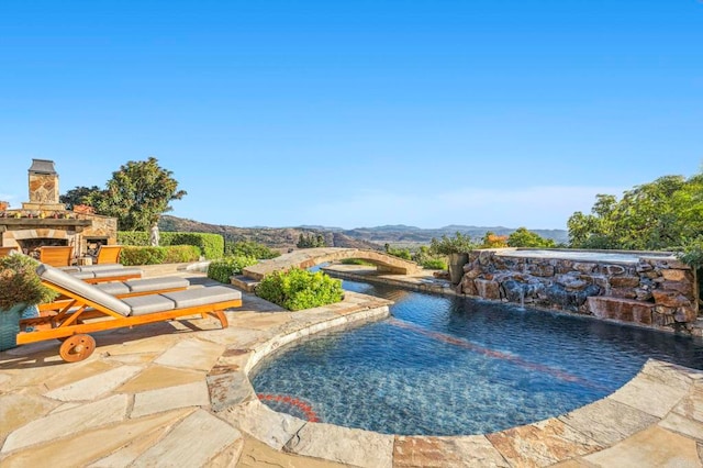 view of pool with pool water feature, an outdoor stone fireplace, a patio area, and a mountain view