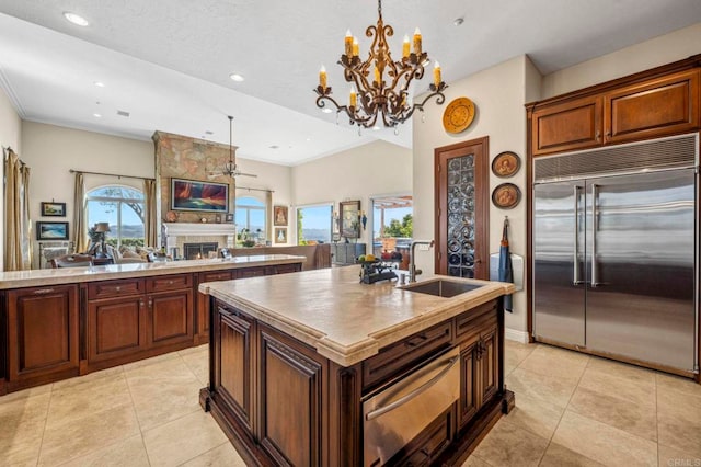 kitchen featuring a kitchen island with sink, sink, light tile patterned floors, a fireplace, and stainless steel built in refrigerator