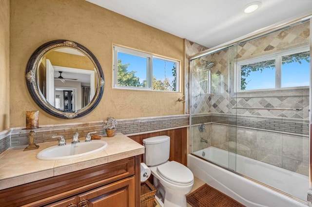 full bathroom with vanity, combined bath / shower with glass door, ceiling fan, toilet, and tile walls