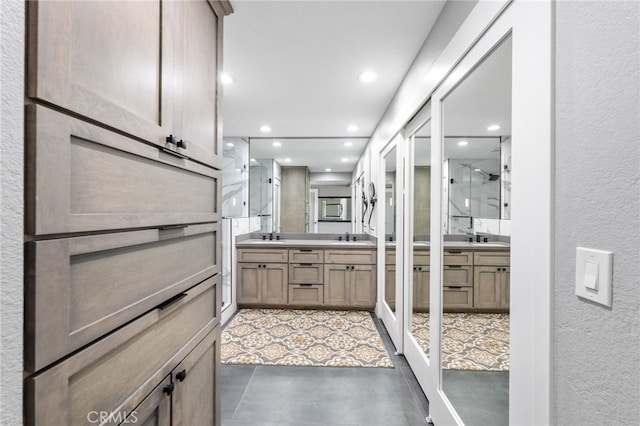 full bathroom with a textured wall, recessed lighting, two vanities, and a shower stall