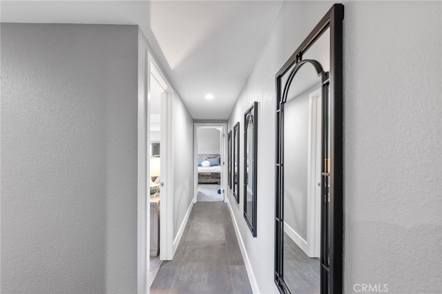 corridor featuring a textured wall, baseboards, and wood finished floors