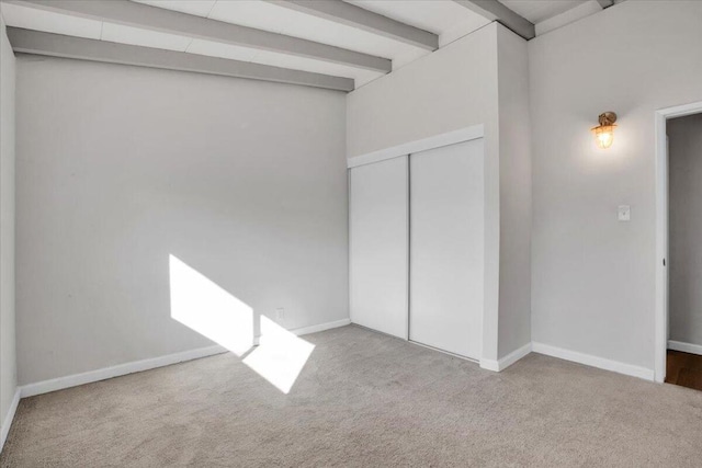 unfurnished bedroom featuring beamed ceiling, light carpet, and a closet