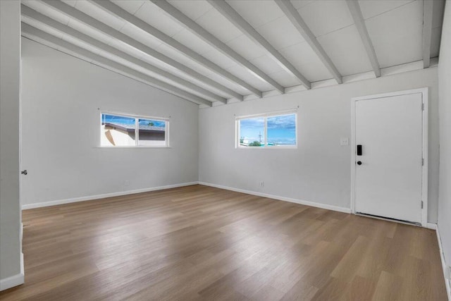 empty room with a wealth of natural light, vaulted ceiling with beams, and light hardwood / wood-style floors