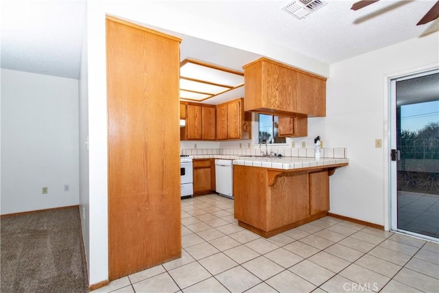 kitchen featuring tile countertops, kitchen peninsula, white dishwasher, range, and sink