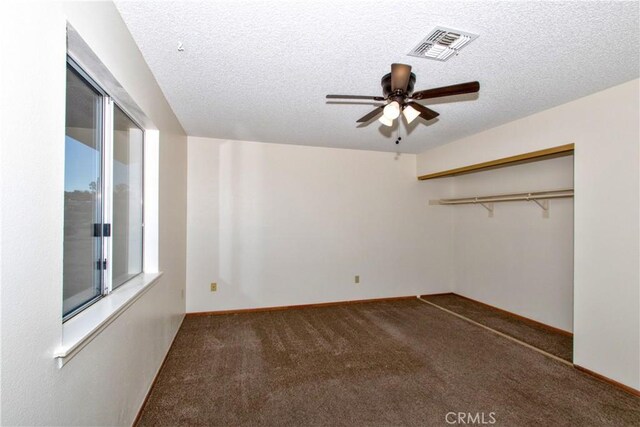 empty room featuring a textured ceiling, ceiling fan, and dark carpet