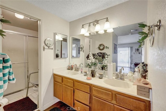 bathroom featuring double vanity, a shower with door, a textured ceiling, and a sink