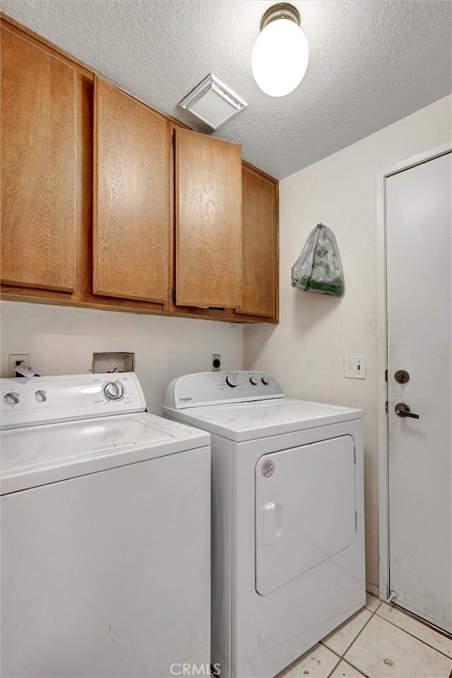 washroom featuring washer and dryer, cabinets, light tile patterned floors, and a textured ceiling