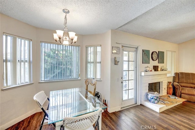dining space featuring wood finished floors, baseboards, a textured ceiling, a brick fireplace, and a chandelier