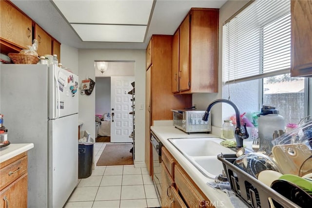 kitchen featuring light countertops, light tile patterned flooring, brown cabinets, and freestanding refrigerator