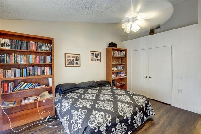bedroom with a ceiling fan, wood finished floors, visible vents, a closet, and a textured ceiling
