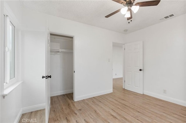 unfurnished bedroom with a textured ceiling, light wood-type flooring, a closet, and ceiling fan