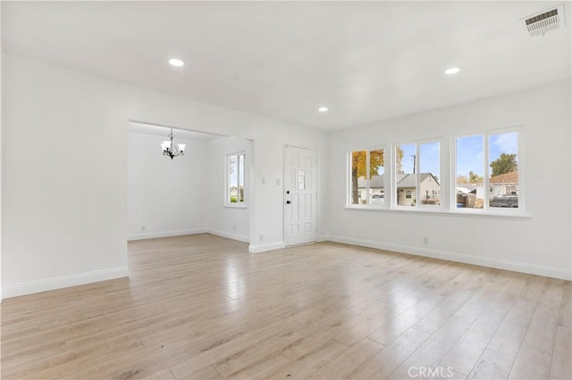 unfurnished living room with light wood-type flooring, a wealth of natural light, and an inviting chandelier