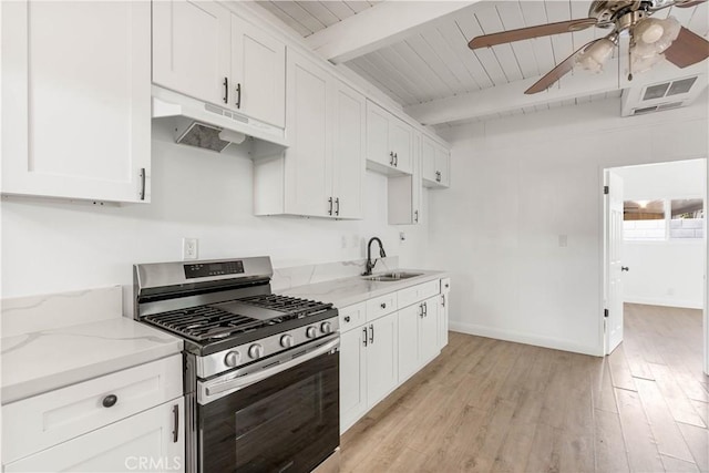 kitchen with beamed ceiling, light stone counters, stainless steel range with gas cooktop, and sink