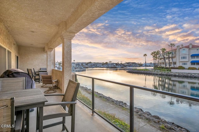 balcony at dusk featuring a water view