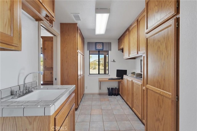 kitchen with light tile patterned floors, tile countertops, and sink