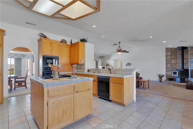 kitchen featuring a wood stove, black appliances, kitchen peninsula, and tile countertops