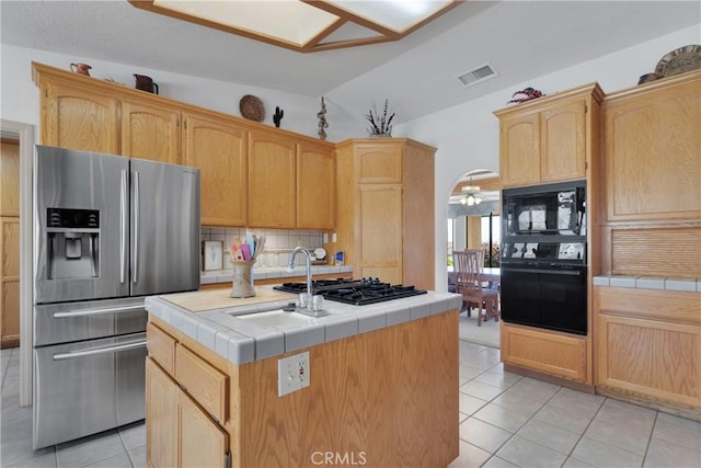 kitchen with light tile patterned floors, tile countertops, a center island, and black appliances