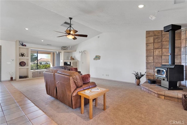 tiled living room featuring ceiling fan, a wood stove, and lofted ceiling