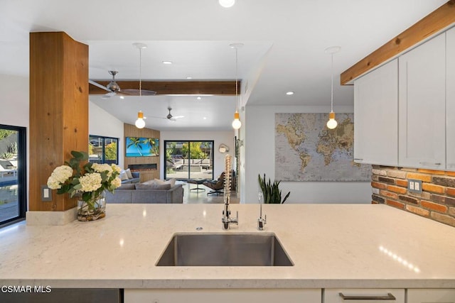 kitchen with sink, light stone counters, beamed ceiling, pendant lighting, and white cabinets