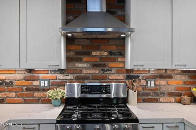 kitchen with white cabinets, wall chimney exhaust hood, light stone counters, and stainless steel range with gas cooktop