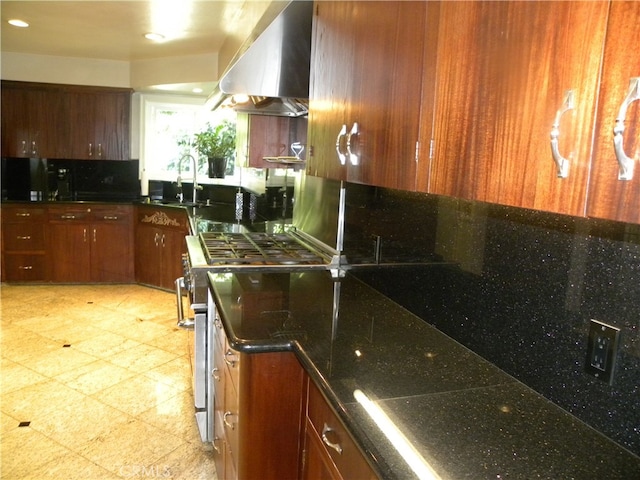 kitchen with wall chimney exhaust hood, sink, dark stone counters, and stainless steel stove