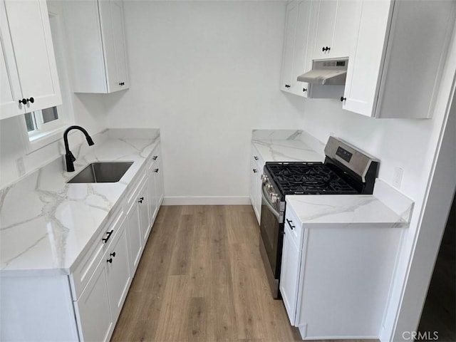 kitchen with stainless steel gas range oven, white cabinets, sink, light wood-type flooring, and light stone counters