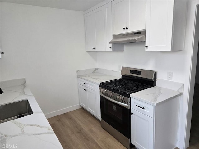 kitchen with stainless steel gas range oven, light wood-type flooring, white cabinetry, and light stone counters