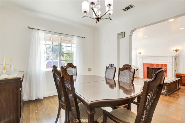 dining room with a brick fireplace, light hardwood / wood-style flooring, and a notable chandelier