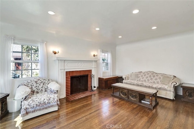 living room featuring a brick fireplace, plenty of natural light, and dark wood-type flooring