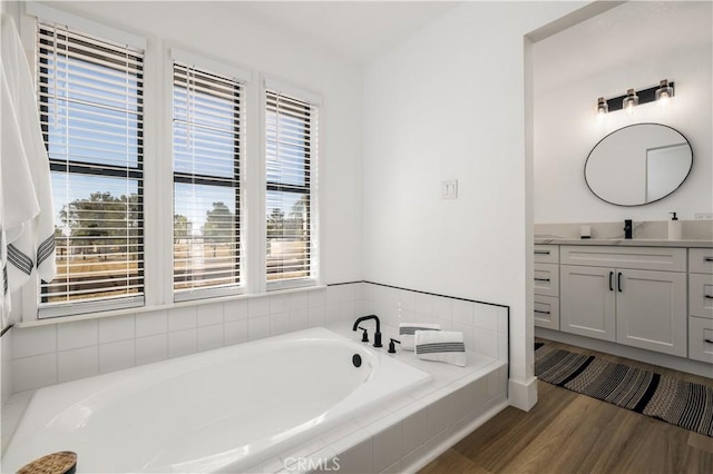 bathroom with vanity, a relaxing tiled tub, and wood-type flooring