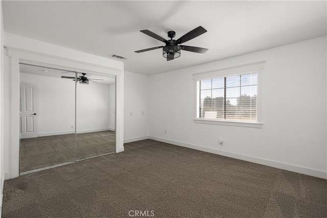 unfurnished bedroom with dark colored carpet, a closet, and ceiling fan