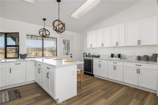 kitchen featuring lofted ceiling, hanging light fixtures, dark hardwood / wood-style flooring, white cabinetry, and beverage cooler