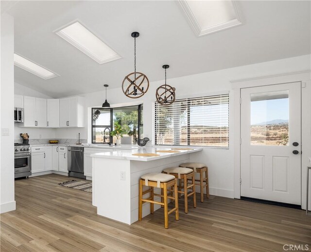 kitchen with white cabinetry, hanging light fixtures, stainless steel appliances, a kitchen breakfast bar, and light hardwood / wood-style floors