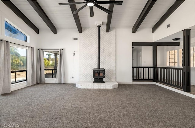 unfurnished living room featuring beam ceiling, a wood stove, ceiling fan, high vaulted ceiling, and carpet floors