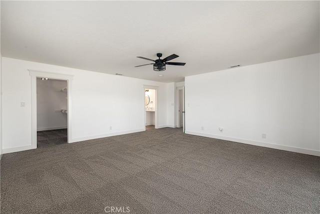 unfurnished bedroom with ensuite bath, a spacious closet, ceiling fan, dark colored carpet, and a closet