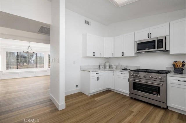 kitchen with white cabinets, stainless steel appliances, hardwood / wood-style flooring, and a chandelier