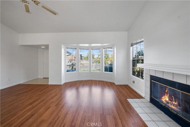 unfurnished living room featuring ceiling fan, a fireplace, vaulted ceiling, and light wood-type flooring