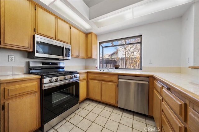 kitchen with appliances with stainless steel finishes, light tile patterned floors, tile counters, and sink