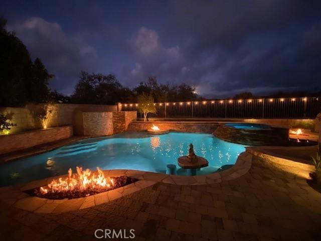 pool at twilight featuring an in ground hot tub and a patio