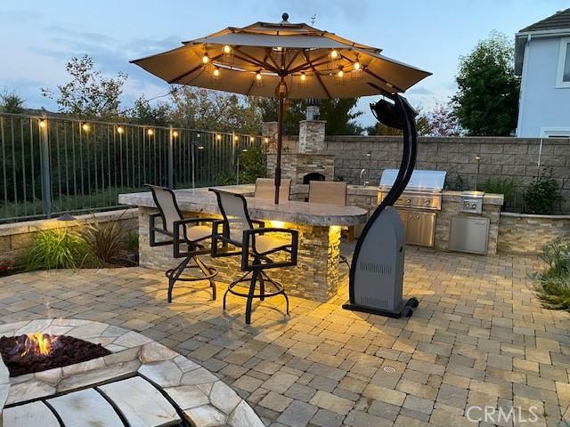 patio terrace at dusk featuring an outdoor bar, grilling area, and an outdoor fire pit