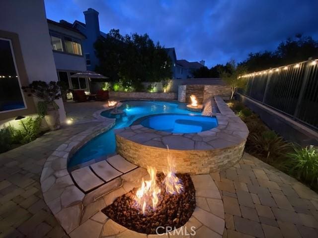 pool at dusk featuring an in ground hot tub, a patio, and a fire pit