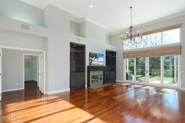 unfurnished living room with hardwood / wood-style flooring, a towering ceiling, ornamental molding, a notable chandelier, and a tiled fireplace