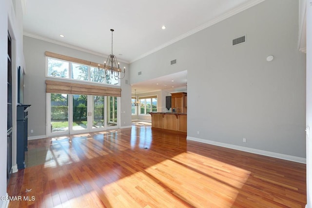 unfurnished living room with a fireplace, crown molding, hardwood / wood-style floors, a chandelier, and a high ceiling