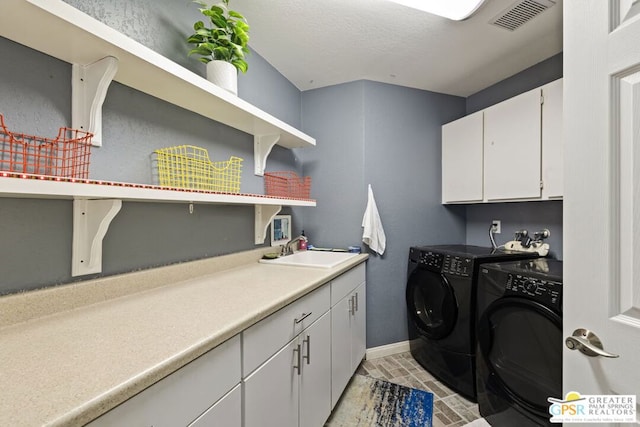 clothes washing area with washing machine and dryer, sink, and cabinets