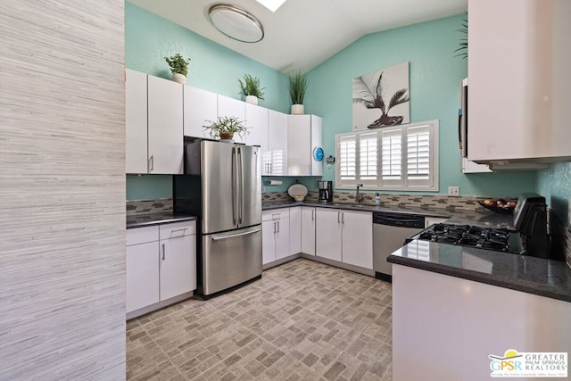 kitchen featuring stainless steel appliances, vaulted ceiling, sink, dark stone countertops, and white cabinetry