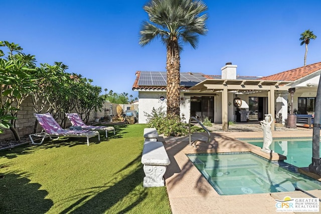 rear view of house with a patio area, a yard, a pool with hot tub, and solar panels