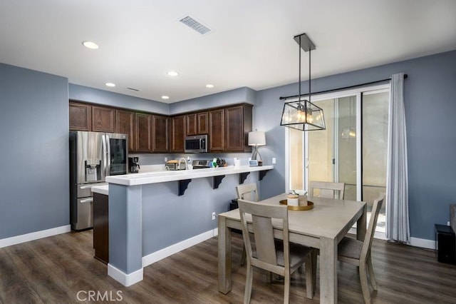 kitchen with a breakfast bar, dark hardwood / wood-style floors, decorative light fixtures, and appliances with stainless steel finishes