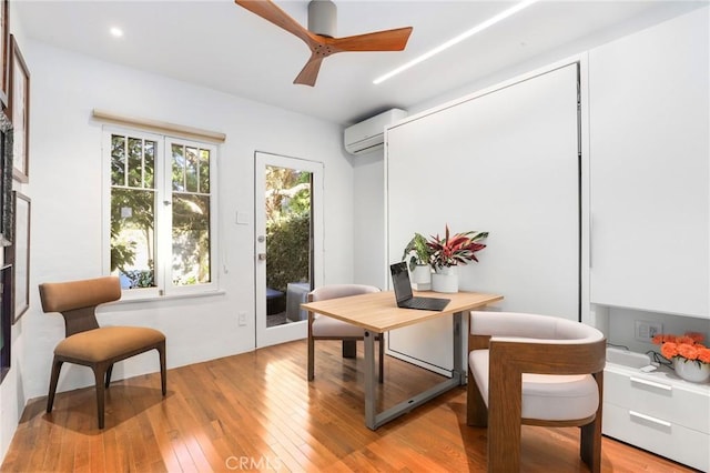 living area featuring a wall mounted AC, ceiling fan, and light hardwood / wood-style flooring