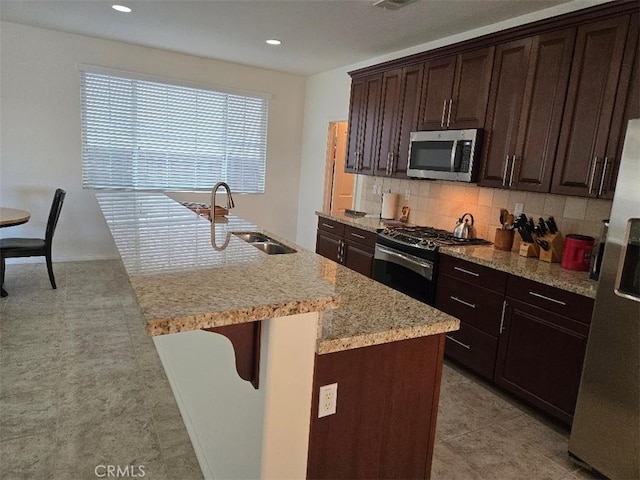 kitchen featuring a kitchen bar, dark brown cabinetry, stainless steel appliances, a kitchen island with sink, and sink